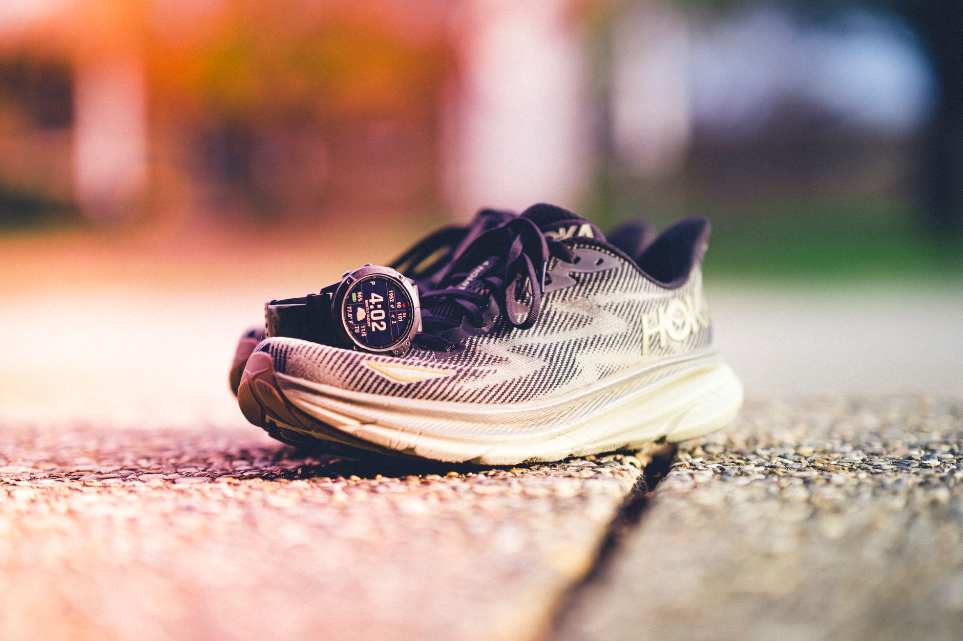 Montre GPS de running affichant l'allure posée contre une chaussure de course au coucher du soleil